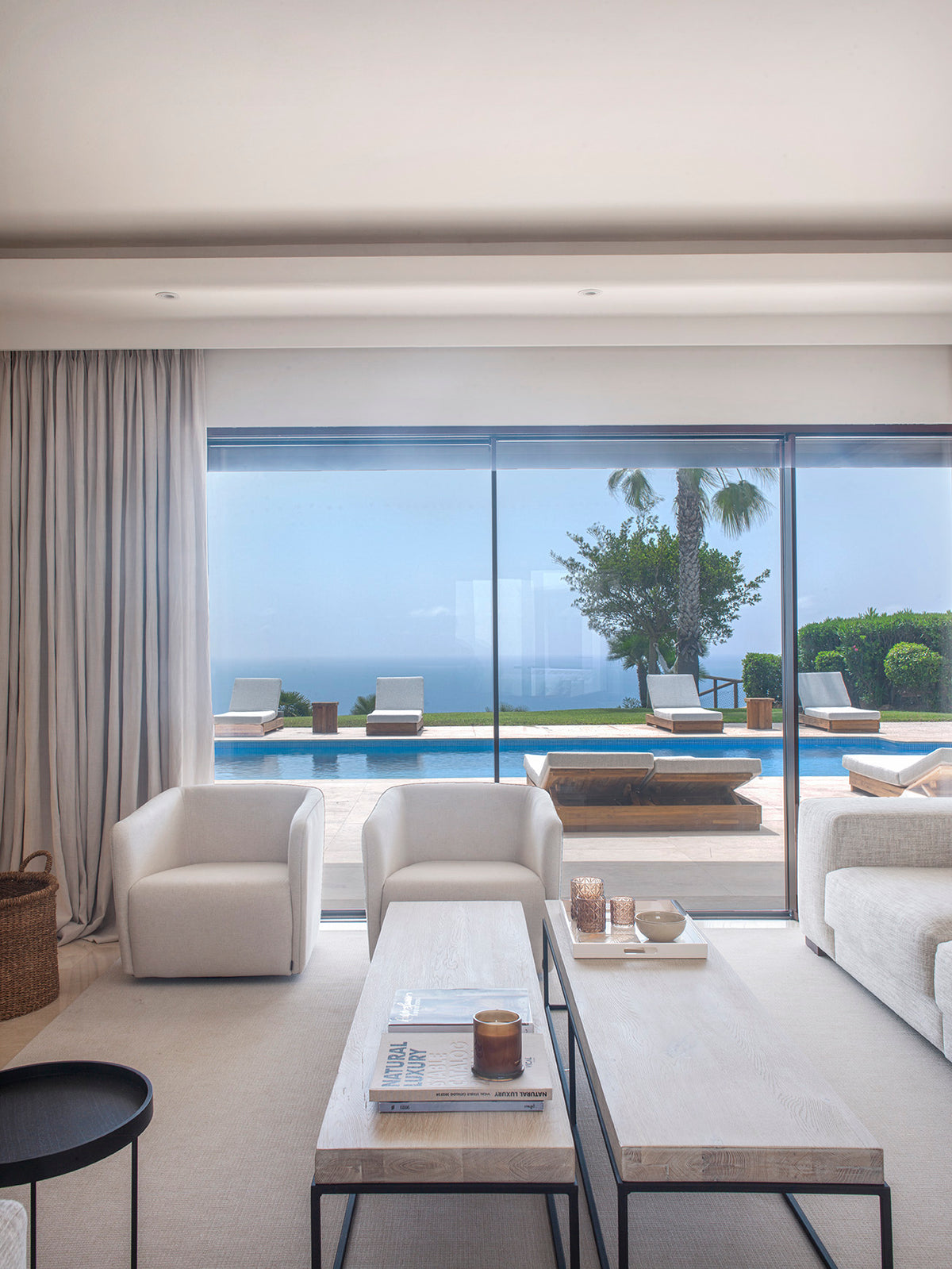Salón con sofás blancos y ventanal con vistas a la piscina y al mar