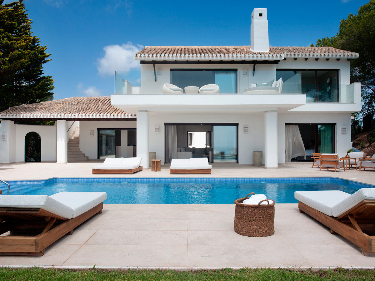 Casa blanca con piscina y tumbonas de madera, proyecto de interiorismo de MUBA
