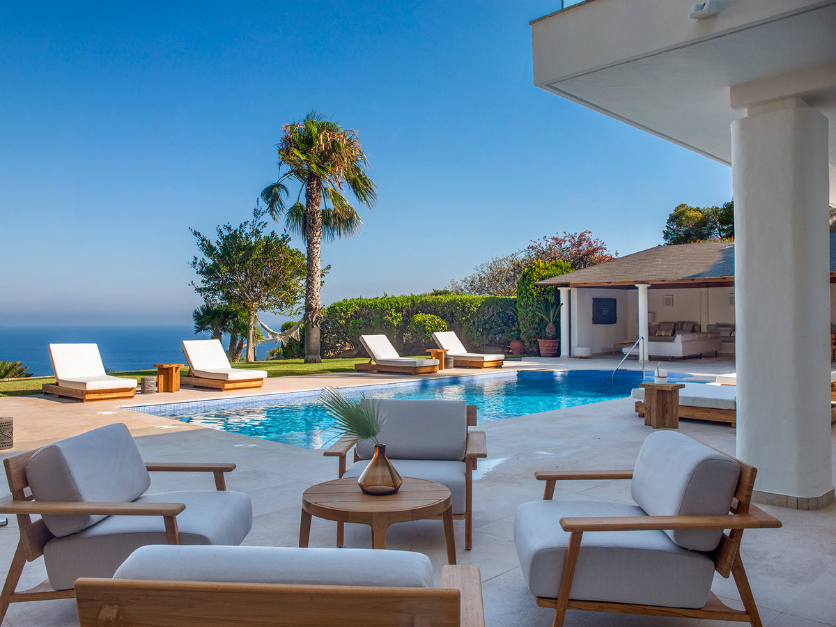 Terraza junto a la piscina con sillones de madera y vistas al mar